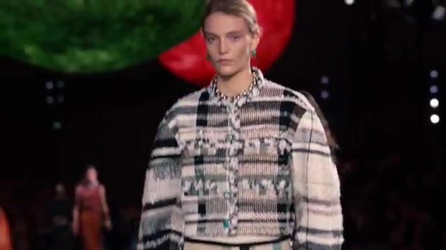 Model in een tweedjasje met bloemen als versiering op de catwalk van Chanel