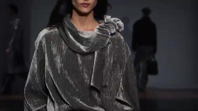 Model in een zilvergrijze, geplisseerde outfit met omgeslagen sjaal op de catwalk van een Emporio Armani-show
