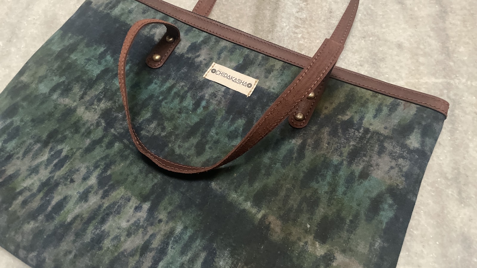 Bruine leren schoudertas en een canvas shopper naast elkaar op een stoel