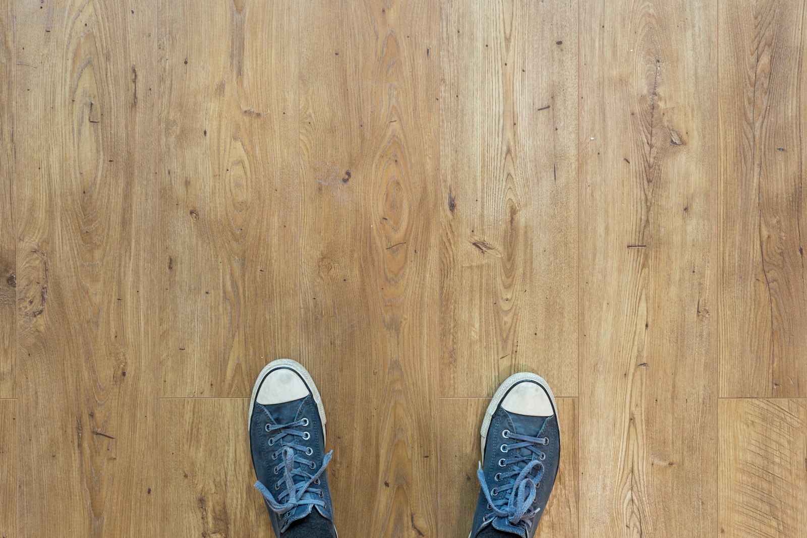 Witte canvas sneakers naast een opgerolde jeans op een houten vloer