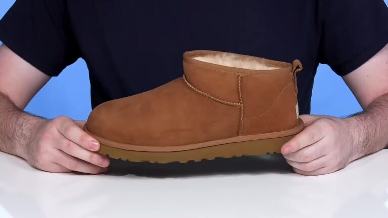 Een lage Ugg Classic Ultra Mini van kastanjebruin schapenvacht, van opzij vastgehouden boven een tafel