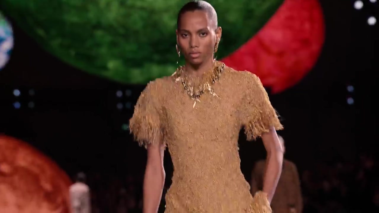 Model in een gouden jurk met franjes voor verlichte planeten tijdens de eerste Chanel-show van Matthieu Blazy