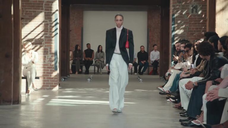 Model in een zwarte jas en wijde witte broek op de catwalk van Calvin Klein Collection lente 2027